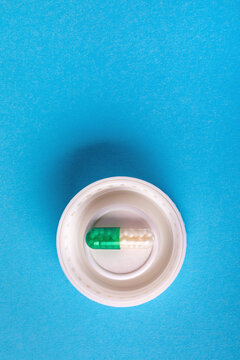 Green and white capsule pill placed inside a white bottle cap on a vibrant blue background, top view, medical and pharmaceutical concept.