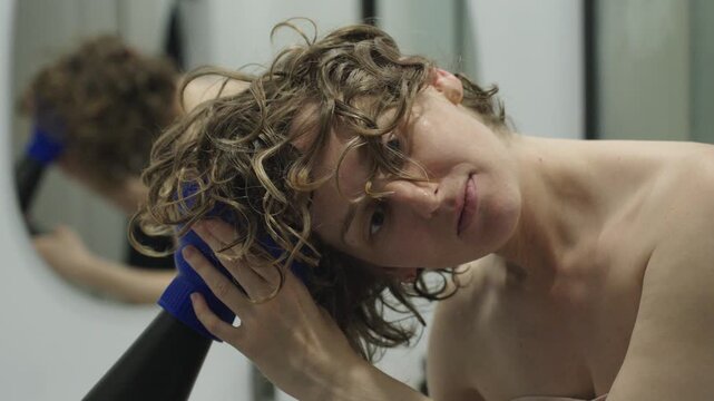 Close up of a woman using a hair dryer with a diffuser attachment to dry and shape her curls in the bathroom. The head is tilted while hands position the diffuser and encourage curl formation. Soft na