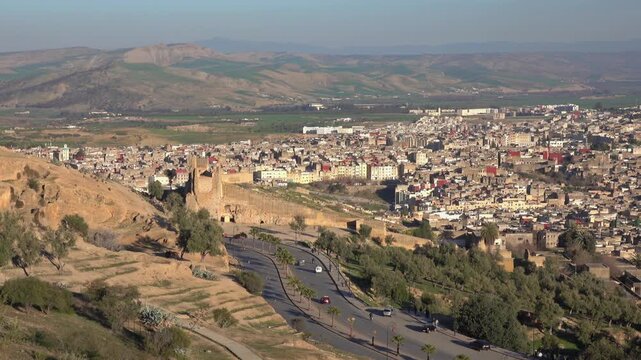 View of the historic Merinid Tombs overlooking the ancient city of Fes with stone fortifications, rolling hills, and urban skyline in Fes, Fez-Meknes, Morocco.