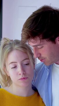 Fatigued caucasian couple standing close together indoors. Tired man with his eyes rolling back in exhaustion, leaning his head on the shoulder and head of his caring girlfriend