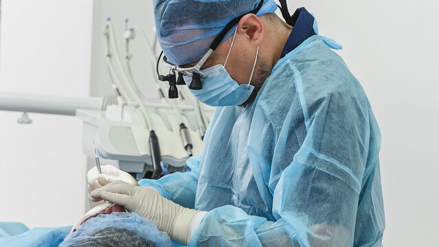 Male patient receiving dental treatment in clinic, mouth open while dentist uses dental drill and operates saliva ejector during procedure
