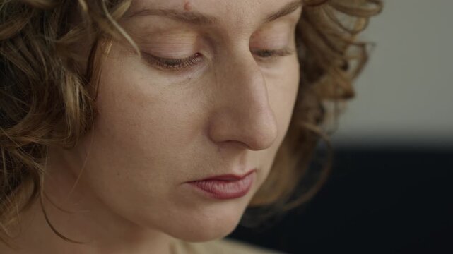 Close up of a woman applying lipstick with a brush. Her mouth is slightly open as she carefully paints the lip line. A compact palette with mirror appears blurred in the background. Soft natural light