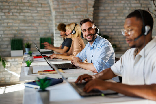 Friendly customer service team working in a modern call center office with headsets and laptops