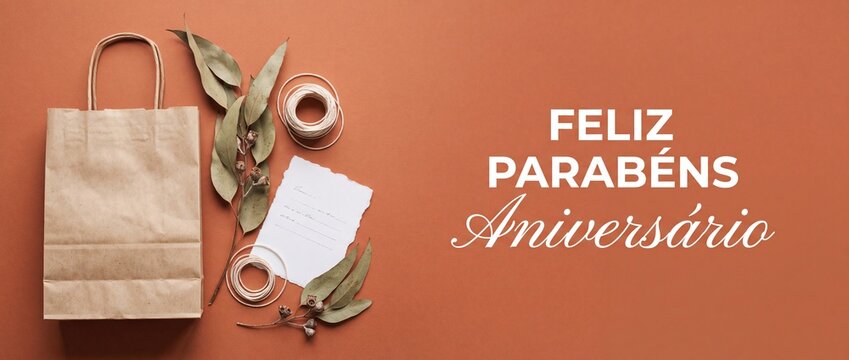 Feliz parabens aniversario birthday gift bag background with eucalyptus leaves, craft card, and ribbon on terracotta background for celebration, holiday greeting banner, and eco friendly present layou