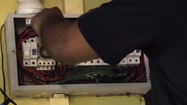 Close up of a professional electrician or technician hands repairing, installing, and maintaining electrical wires and miniature circuit breakers (MCB) inside a home distribution board box panel.