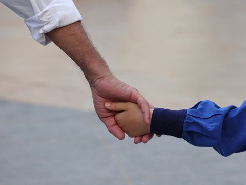 Vue rapproch&eacute;e du bras d'un homme en chemise blanche donnant la main &agrave; celle d'une enfant portant une chemise bleu>. Symbole amiti&eacute; inter g&eacute;n&eacute;ration.