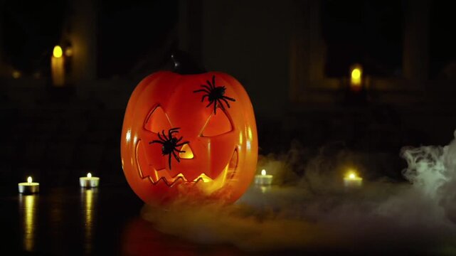 A bright orange Halloween pumpkin (jack-o'-lantern) glows in the darkness, adorned with two black spiders on its surface. 