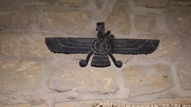 View of a carved stone Faravahar symbol mounted on an ancient limestone wall in the historic district of Baku, Baku, Azerbaijan.
