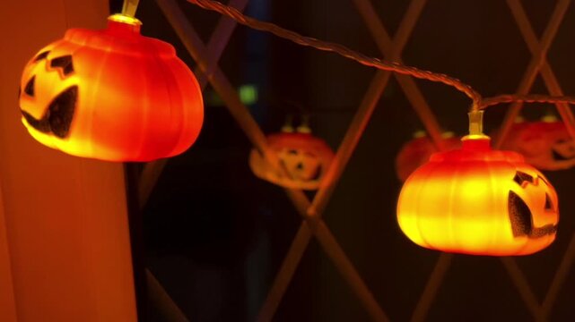 A close-up shot capturing the warmth and festive atmosphere of Halloween-themed decorative lights, featuring a string of glowing jack-o'-lantern-shaped LED lights against the darkness of the night.