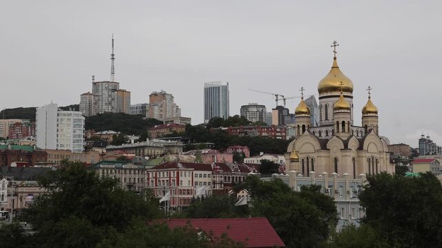 View of the golden-domed Pokrovsky Cathedral set against the urban skyline and hills of Vladivostok, Primorsky Krai, Russia.