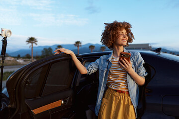 Young woman with curly hair stands beside a car, wearing a denim jacket over a striped shirt and mustard skirt, smiling while checking her phone. © SHOTPRIME STUDIO