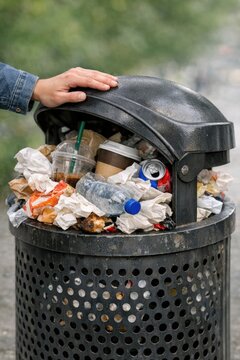 A person struggling to access a trash can filled with garbage, highlighting the issue of waste management and sustainability