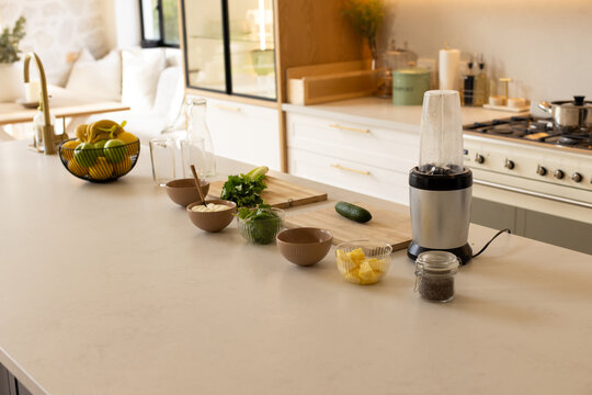 Kitchen island countertop is showing personal blender, bowls, cutting board with herbs near window