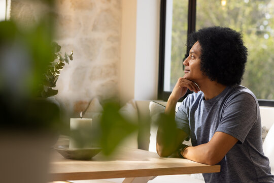 Adult African American man sitting at table, gazing toward window with green candle, copy space