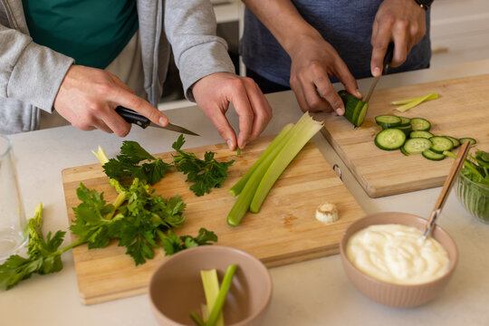 African American men chopping parsley and slicing cucumber on kitchen counter with cutting boards