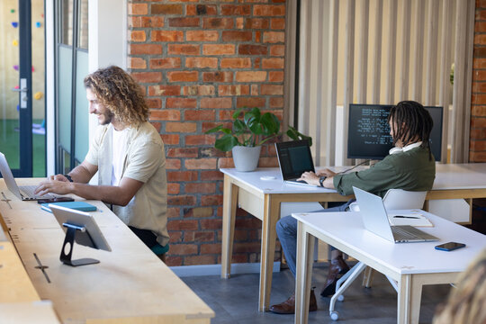 Diverse male coworkers working in open office left man typing laptop right coding screen