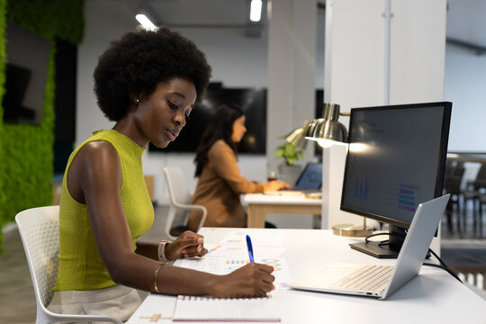 Staff working in office, African-American woman in lime top writing charts with blue pen