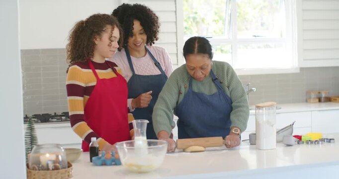 African family senior woman placing dough and rolling with wooden pin at white island, teaching