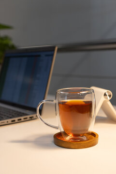 Double-wall mug with amber tea on white desk coaster, laptop left showing table