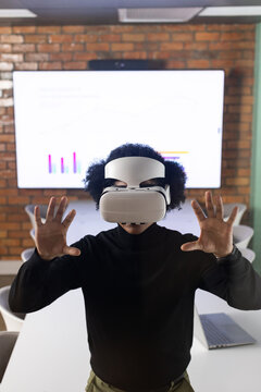 Man of African descent standing at conference table wearing white VR headset, viewing display