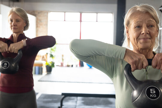 Mature women lifting 5 KG kettlebells in studio, senior on right holding upright row, copy space