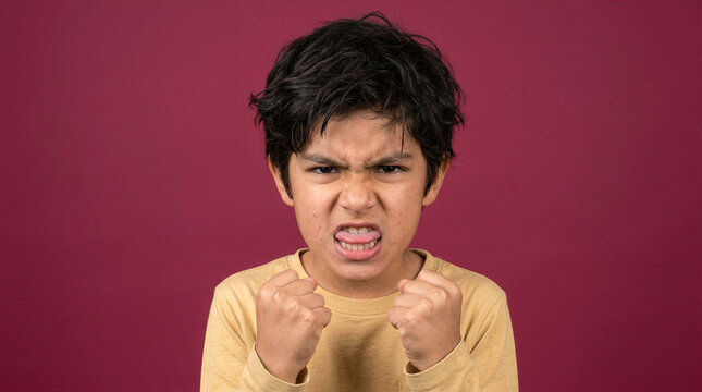 Young boy makes a frustrated face, clenching fists and sticking out his tongue