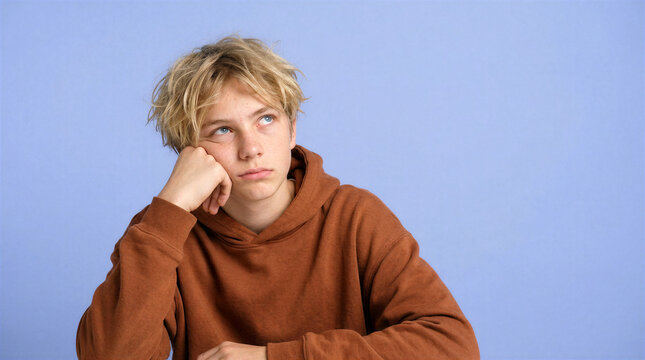 Teenage boy with blonde hair rolls his eyes in boredom against a blue background