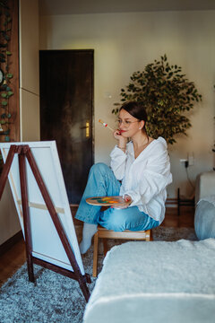 Young woman painting with easel at home