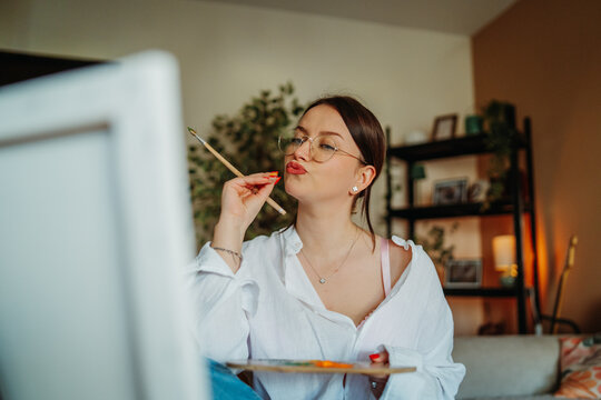 Woman artist holding paintbrush pouting for selfie portrait