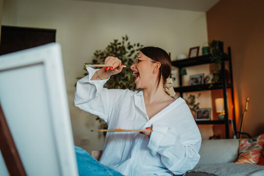 Happy woman artist singing while painting at home