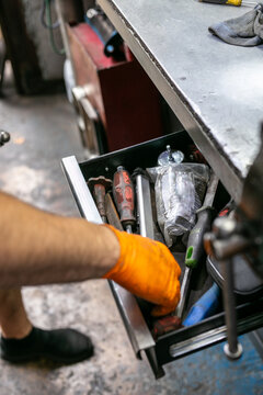 Mechanic selecting or picking up a tool from an open workbench drawer containing a selection of hand tools, hardware, and automotive parts in a small auto repair workspace. The practical garage scene 