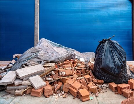 pile of construction debris including bricks concrete drywall and a black trash bag next to a blue tarp and clear plastic sheeting waste rubble demolition building materials