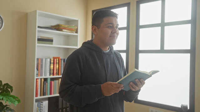 Man holding open book and reading while standing by bookshelves in a library building; study concentration.