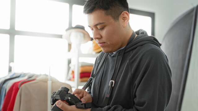 Man photographer checking camera touchscreen and adjusting settings in studio with clothing rack, mannequin and softbox visible; concentration.