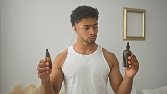 Man holding two dropper bottles and comparing labels in studio while inspecting amber glass for use; uncertainty selfcare routine.