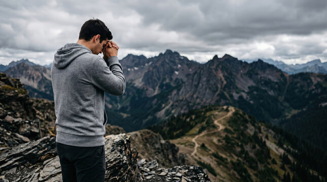 Man praying on top of mountain. Religious person standing on cliff edge, looking at distant peaks with hands clasped. Spiritual connection with nature, hope and faith concept.
