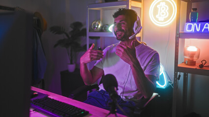 Man wearing headset gesturing hands toward monitor and pointing while seated at computer in a...
