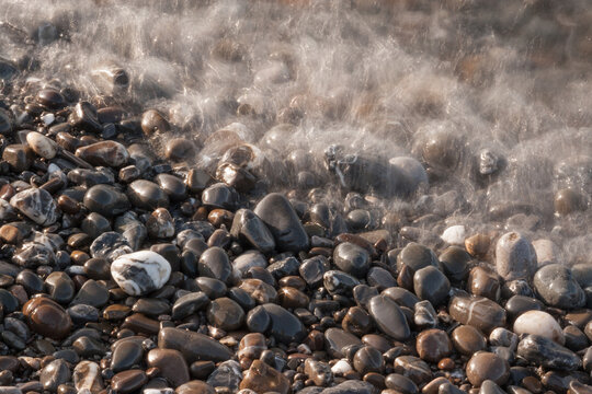 Long exposure close up of sea wave motion over smooth wet pebbles