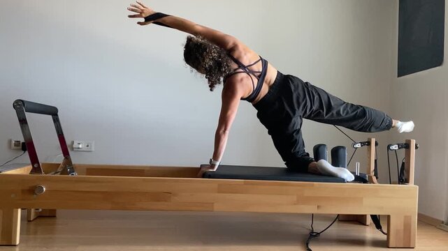 FİT WOMAN , EXERCİSİNG ON REFORMER PİLATES MACHİNE, ARM AND LEG EXTENSİON EXERCİSE İN BRİGHT STUDİO 

