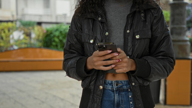 Young woman holding smartphone and texting, hands and midriff visible on an urban street; calm connection.