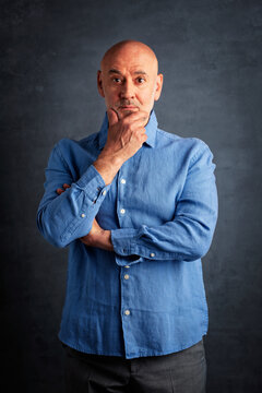 A middle-aged man standing against a dark background, looking surprised