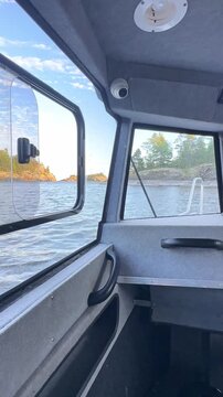 Interior view of a boat cabin with open window, showcasing the serene lake and rocky shoreline in the background under a clear blue sky