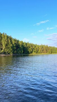 Serene lake view surrounded by lush green forest under a clear blue sky. Boat trip on Lake Ladoga. Ladoga skerries, Sortavala, Karelia. Landscape. Honkasalo Island.