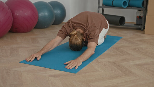 Man on yoga mat performing gentle backbend with hands pressed to wooden floor in studio; calm concentration.