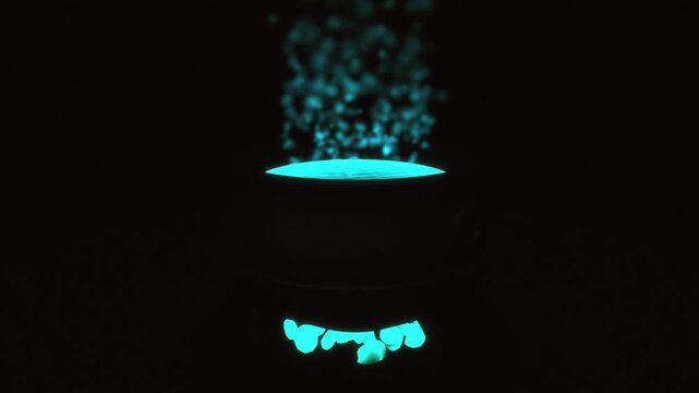 Witch cauldron boiling with luminous cyan magic potion and rising floating particles in a dark atmospheric environment 3D animation