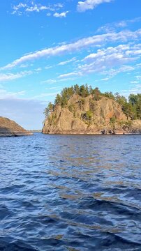 Scenic view of calm water between rocky cliffs and trees under a clear blue sky in a natural landscape. Boat trip on Lake Ladoga. Ladoga skerries, Sortavala, Karelia. Landscape. Honkasalo Island.