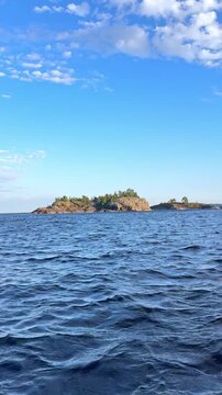 Scenic view of calm water between rocky cliffs and trees under a clear blue sky in a natural landscape. Boat trip on Lake Ladoga. Ladoga skerries, Sortavala, Karelia. Landscape. Honkasalo Island.