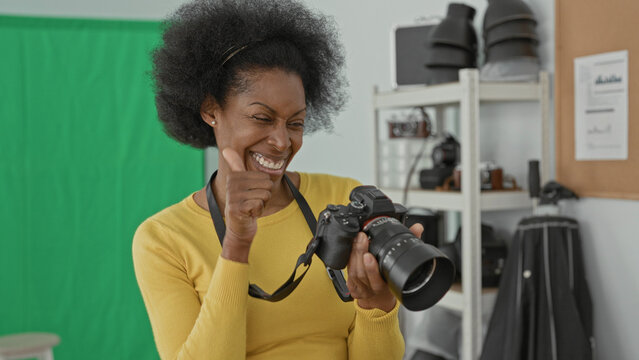 Woman smiling while inspecting a dslr camera, hands on controls and fist pump visible in a green screen studio; creative joy.