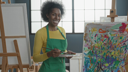 Woman painter holds brush and palette while smiling, hand poised to paint in a bright art studio  creativity joy expression. © Krakenimages.com