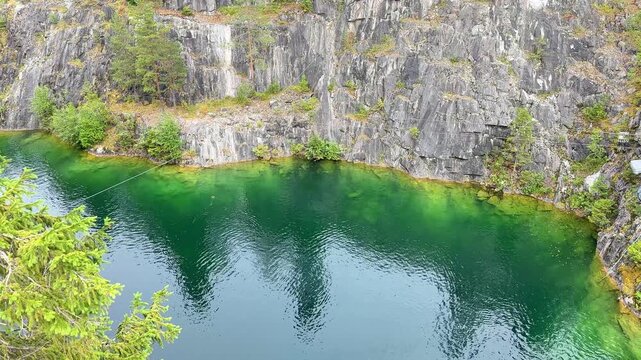Ruskeala Mountain Park in Karelia. Marble Canyon. Summer Day. Scenic view of a tranquil green lake surrounded by rocky cliffs and lush trees in a natural landscape.